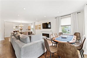A living room with a sofa, chairs, a coffee table, a fireplace, a TV, and a window with curtains. - LUX 4BR Somerville, Steps to Green Line, Free Parking, Game Room+Poker Table (Somerville)