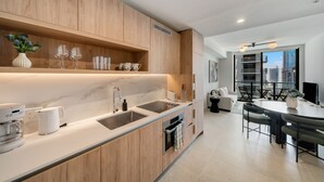 A modern kitchen with wooden cabinets, a built-in oven, and a dining area with a table and chairs. - Crosby Miami WTC 1BR/1BA Cool Residence #2210 (Miami)