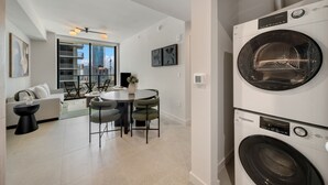 A modern apartment with a dining area, a sofa, a table, and a large window with a city view. - Crosby Miami WTC 1BR/1BA Cool Residence #2210 (Miami)