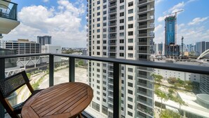 A balcony with a wooden table and chairs, overlooking a cityscape with high-rise buildings and construction cranes. - Crosby Miami WTC 1BR/1BA Cool Residence #2210 (Miami)