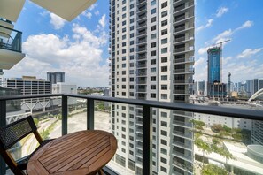 Ein Balkon mit einem Holztisch und Stühlen, der auf einen Stadtblick mit Hochhäusern und Baukränen blickt.