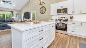 A modern kitchen with white cabinetry, a large island, a built-in oven, and a ceiling fan. - Carolina Meadows w/ Hot tub (Weaverville)