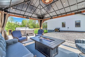 Eine überdachte Terrasse mit Gartenmöbeln, einem Feuerkorb und Blick auf ein Haus.