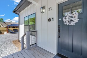 Ein Haus mit einer dunklen Haustür, der Nummer 21 darüber, einer kleinen Veranda mit Geländer und einem Fenster.