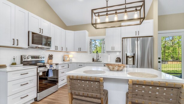 A modern kitchen with white cabinetry, a large island with barstools, a built-in oven, and a stainless steel refrigerator. - Carolina Meadows w/ Hot tub (Weaverville)