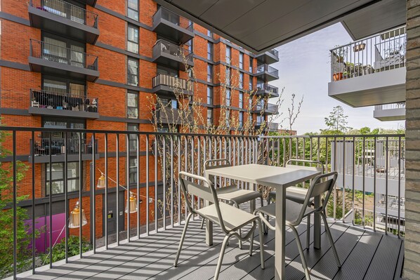 A balcony with a table and chairs, a railing, and a view of a brick building with balconies. - Modern City Elegance (London)