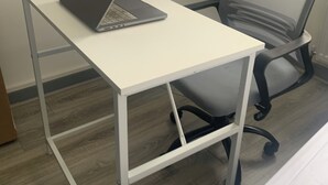 Una scrivania bianca con un portatile, una sedia da ufficio a rete e una scala sullo sfondo.