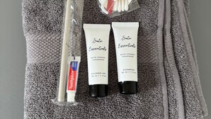 Un asciugamano grigio con articoli da toilette, tra cui uno spazzolino, dentifricio e due flaconi di shampoo e bagnoschiuma.