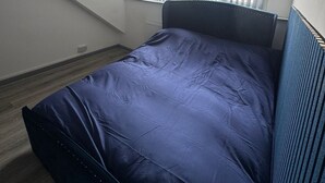 Una camera da letto con un letto, una finestra con persiane, un soffitto spiovente e una lampada a vista.