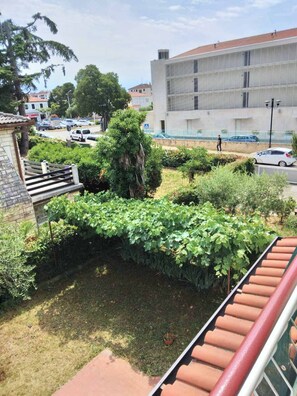 A courtyard with a garden, a building with a tiled roof, and a street with parked cars. - Apartment 2427/205552 (Istria - Umag), 700m from the beach (Umag)
