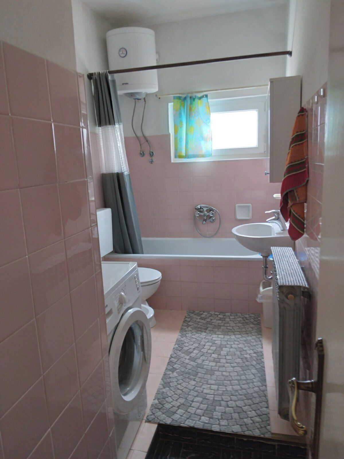A compact bathroom with a washing machine, toilet, bathtub, and a small window with a curtain.