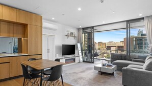 Una sala de estar moderna con comedor, televisor de pantalla plana y un ventanal con vistas a la ciudad.