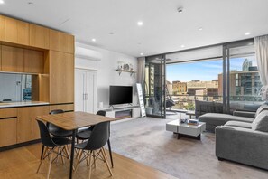 A modern living room with a dining area, a flat-screen TV, and a large window offering a city view. - Chic 1-Bed Apartment with Secure Parking (Auckland City)