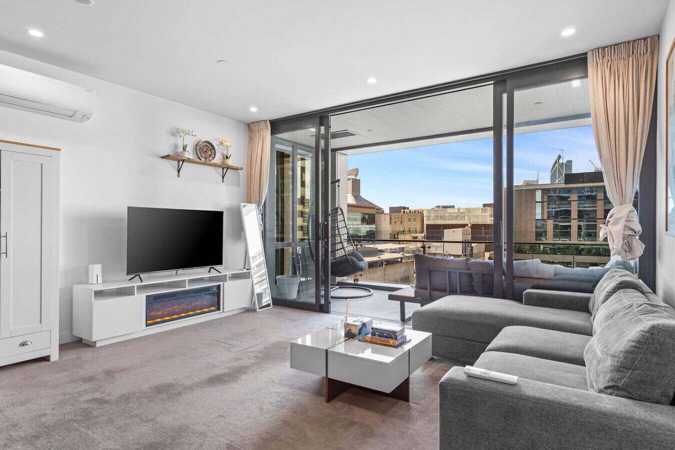 Ein modernes Wohnzimmer mit Flachbildfernseher, einer Couch, einem Couchtisch und einem großen Fenster mit Blick auf die Stadt.
