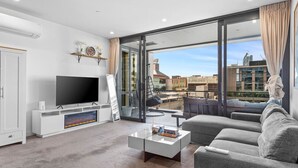 Una sala de estar moderna con una televisión de pantalla plana, un sofá, una mesa de centro y un amplio ventanal con vistas a la ciudad.