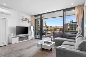 A modern living room with a flat-screen TV, a sofa, a coffee table, and a large window offering a city view. - Chic 1-Bed Apartment with Secure Parking (Auckland City)