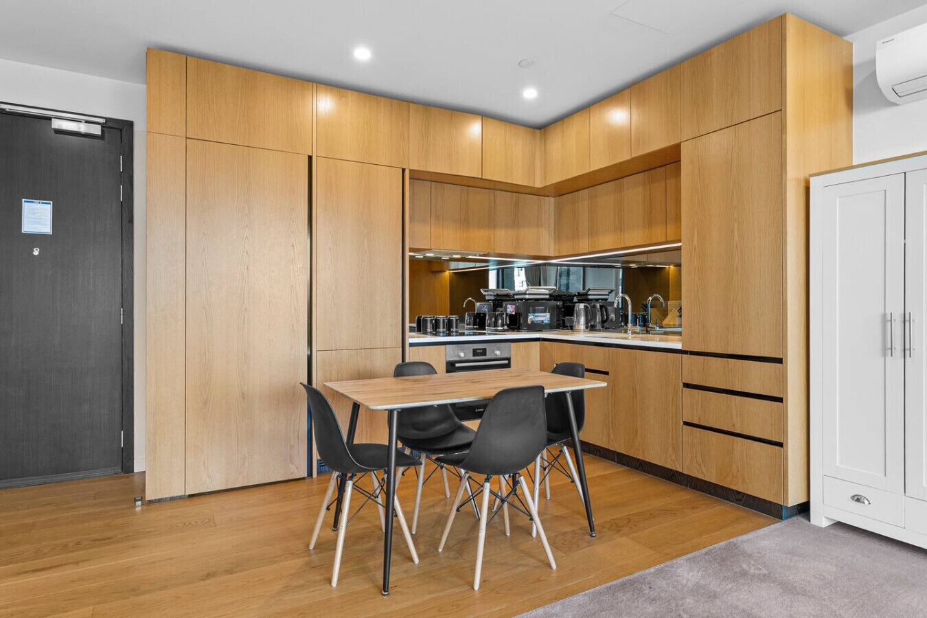 Una cocina compacta con zona de comedor, armarios de madera y una puerta blanca.