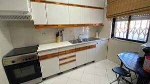 A kitchen with white cabinets, a stove, a sink, and a window with blinds. - 2-bedroom Quarteira apartment near the beach. (Quarteira)