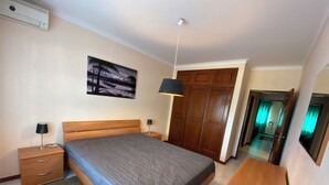 A bedroom with a bed, bedside tables, a desk, a wardrobe, and a painting on the wall. - 2-bedroom Quarteira apartment near the beach. (Quarteira)