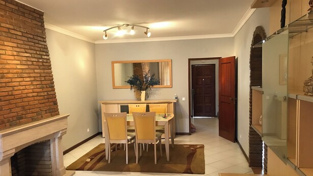A dining area with a brick fireplace, a dining table with chairs, a mirror, and a door leading to another room. - 2-bedroom Quarteira apartment near the beach. (Quarteira)