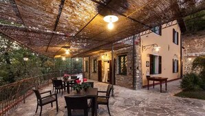 Eine Außenpatio mit Steinboden, einem Tisch mit Stühlen und einem überdachten Sitzbereich mit gewebtem Dach.