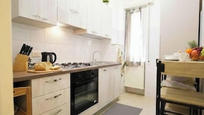 Una cocina moderna con armarios blancos, horno empotrado, estufa a gas y un pequeño comedor con mesa y sillas.