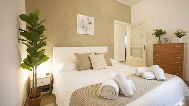 Un dormitorio ordenado con cama, mesitas de noche, cómoda y una planta en maceta.