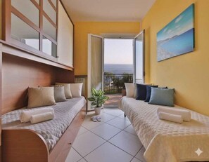 Quarto de hotel com duas camas, uma planta em vaso e uma varanda com vista.