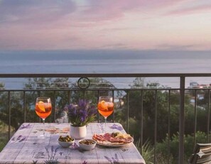 Mesa posta com bebidas e comida em varanda com vista para o mar.
