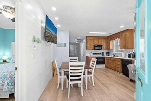 A compact kitchen with wooden cabinets, a dining table with chairs, and a refrigerator. - 7031 Lobster Lane - Golf Cart Included (Myrtle Beach)