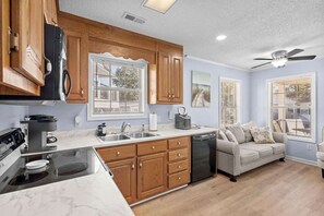 A compact kitchen with wooden cabinets, a dishwasher, and a dining area with a sofa. - 7031 Lobster Lane - Golf Cart Included (Myrtle Beach)