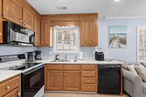 A compact kitchen with wooden cabinets, a microwave, stove, and dishwasher. - 7031 Lobster Lane - Golf Cart Included (Myrtle Beach)