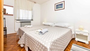 Quarto com duas camas, janela com cortinas, radiador, mesa de cabeceira com abajur e quadro na parede.