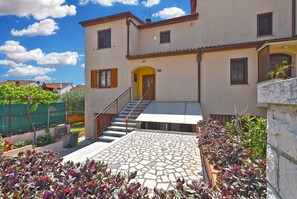 A building with a staircase leading to a door, a tiled patio, and a garden with various plants. - Holiday apartment with terrace and barbecue (Pula)