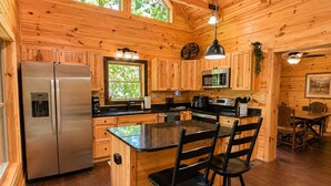 A wooden cabin interior with a kitchen featuring a refrigerator, microwave, and bar stools. - Mountain Birdies Log Cabin In Rumbling Bald at Lake Lure! Golf Views! Work Space (Lake Lure)