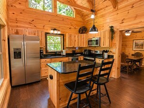 A wooden cabin interior with a kitchen featuring a refrigerator, microwave, and bar stools.