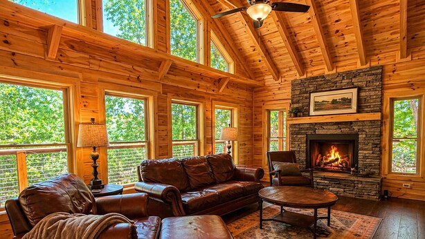 A log cabin interior with a stone fireplace, leather furniture, and large windows. - Mountain Birdies Log Cabin In Rumbling Bald at Lake Lure! Golf Views! Work Space (Lake Lure)