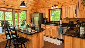 A wooden cabin interior with a kitchen island, bar stools, and a view of the outdoors. - Mountain Birdies Log Cabin In Rumbling Bald at Lake Lure! Golf Views! Work Space (Lake Lure)