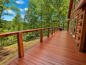 Une terrasse en bois avec une rambarde, entourée d’arbres et sous un ciel dégagé.