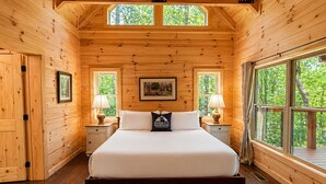 A wooden cabin bedroom with a bed, two nightstands, two lamps, a framed picture, and a window with a view of trees. - Mountain Birdies Log Cabin In Rumbling Bald at Lake Lure! Golf Views! Work Space (Lake Lure)