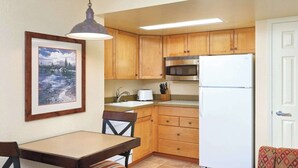 A compact kitchen with wooden cabinets, a white refrigerator, a microwave, a sink, and a dining area with a table and chairs. - WorldMark Canmore-Banff - 1 BR (Canmore)