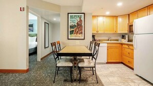 A hotel room with a dining table, chairs, a kitchen area with wooden cabinets, a refrigerator, and a poster on the wall. - WorldMark Canmore-Banff - 1 BR (Canmore)