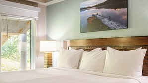 A hotel room with a large bed, a wooden headboard, a nightstand with a lamp, and a painting of a lake. - WorldMark Canmore-Banff - 1 BR (Canmore)