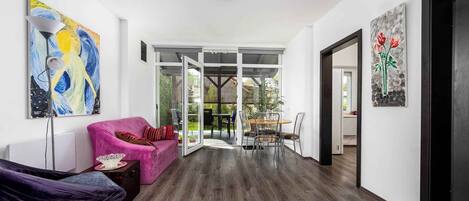 A spacious living area with a modern design, featuring a pink sofa, a dark armchair, and a dining table with chairs.