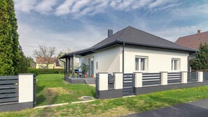 Ein modernes, zweistöckiges Haus mit überdachter Veranda, einem eingezäunten Garten und blauem Himmel.