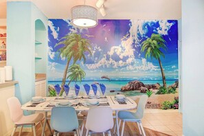 Ein Essbereich mit einer Wandmalerei einer Strandansicht, einer Chandelüster und einem für vier Personen gedeckten Tisch.
