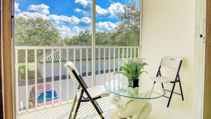 A balcony with two chairs, a glass table, and a potted plant. - Bright 3BR Resort Condo Near Disney with Pool, Gym, Balcony (Kissimmee)