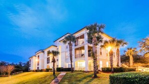 A multi-story building with balconies, surrounded by well-maintained lawns and palm trees. - Bright 3BR Resort Condo Near Disney with Pool, Gym, Balcony (Kissimmee)
