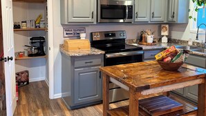 A kitchen with grey cabinets, a black microwave, a wooden table, and a countertop with various items.