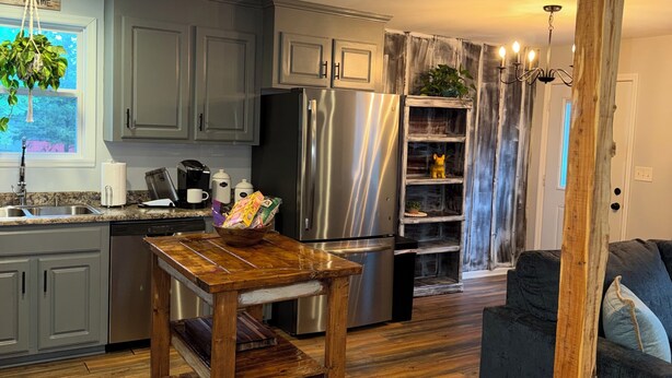 A modern kitchen with grey cabinets, stainless steel appliances, a wooden table, and a dark grey sofa.